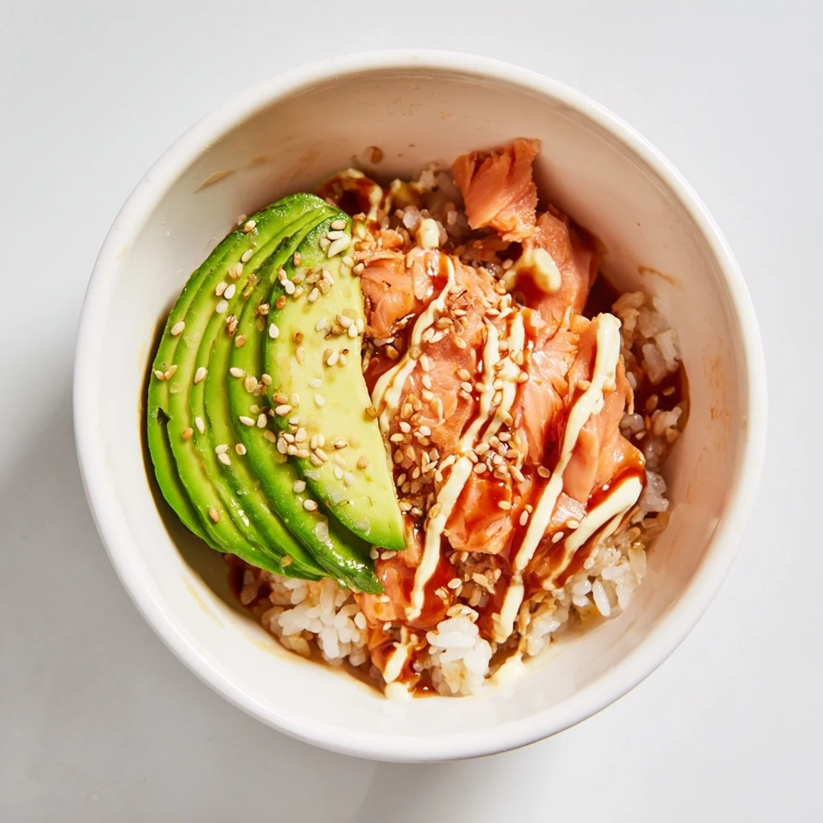 Flaked salmon and creamy avocado top seasoned rice in this Emily Mariko Salmon Rice Bowl, drizzled with spicy mayo.