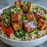 A vibrant bowl of quinoa vegetable teriyaki with golden tofu cubes and sesame garnish.