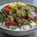 Juicy teriyaki chicken pieces and crisp vegetables sit atop steamed jasmine rice, garnished with scallions and toasted sesame seeds.