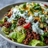 Close-up of a Healthy Taco Bowl drizzled with lime yogurt crema, topped with radishes, cilantro, and shredded cheddar cheese.