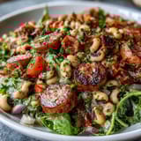 A close-up of Hoppin John Style Black-Eyed Pea Salad plated over crisp mixed greens, featuring cherry tomatoes and celery drizzled with tangy tarragon dressing.