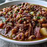 Close-up of simmering Black-Eyed Pea Stew with Smoked Ham Hocks, showcasing tender vegetables and shredded ham in a rich, savory broth.