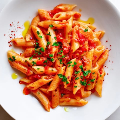 Steaming plate of Penne all'Arrabbiata: vibrant red sauce coats perfectly cooked penne pasta.