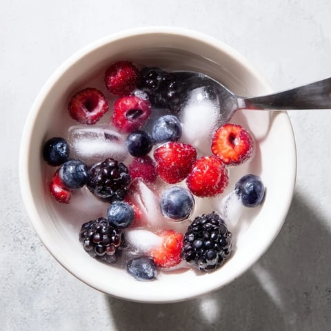 A close-up of Nature's Cereal Bowl with chilled coconut water poured over vibrant mixed berries and ice cubes.  