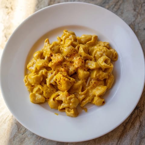 A close-up of a bowl of One-Pot Butternut Squash Mac & Cheese, garnished with fresh, green herbs.