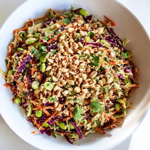 Bright serving of Crunchy Thai Peanut Salad, featuring vibrant purple cabbage and red bell pepper, tossed in a tangy peanut sauce with lime wedges on the side.