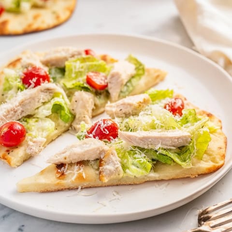 Sliced grilled chicken and crisp romaine on a warm Chicken Caesar Flatbread with parmesan.