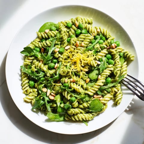 Spring Green Pesto Pasta Salad in a rustic bowl, featuring vibrant pesto-coated fusilli, tender peas, fresh arugula, and crunchy toasted pine nuts, ready to serve.