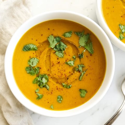Vibrant orange butternut squash and lentil soup in a white ceramic bowl, topped with parsley and a drizzle of olive oil.  