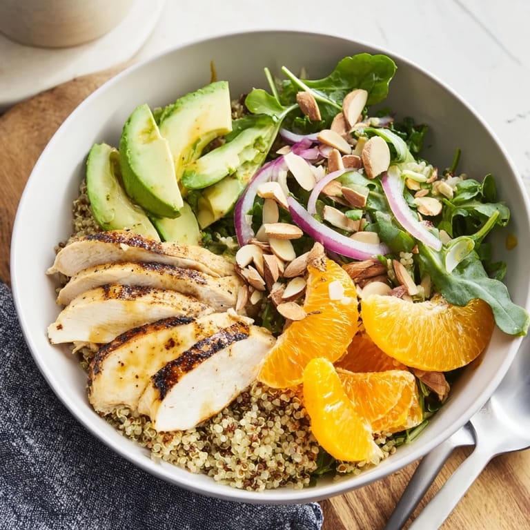 A close-up of a Citrus Herb Chicken Salad Bowl shows creamy avocado, bright orange slices, and toasted almonds.
