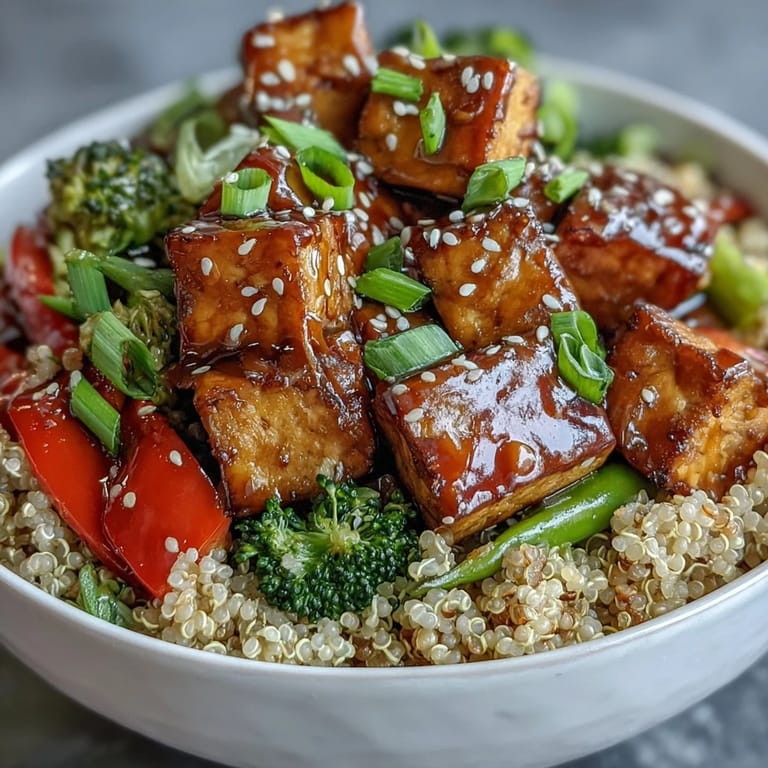 A vibrant bowl of quinoa vegetable teriyaki with golden tofu cubes and sesame garnish.