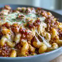 Creamy beef and cheese One-Pan High Protein Chili Mac topped with green onions in a rustic bowl.