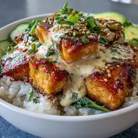 A vibrant bowl of salmon cubes over fluffy rice, drizzled with creamy spicy mayo and garnished with cucumber and sesame seeds.